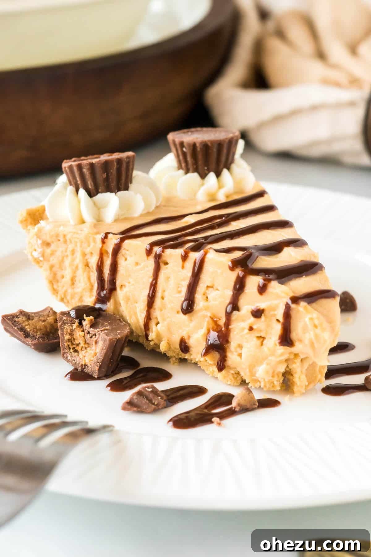A delectable slice of no bake peanut butter pie, drizzled with rich chocolate sauce and topped with mini Reese's cups, ready to be enjoyed.