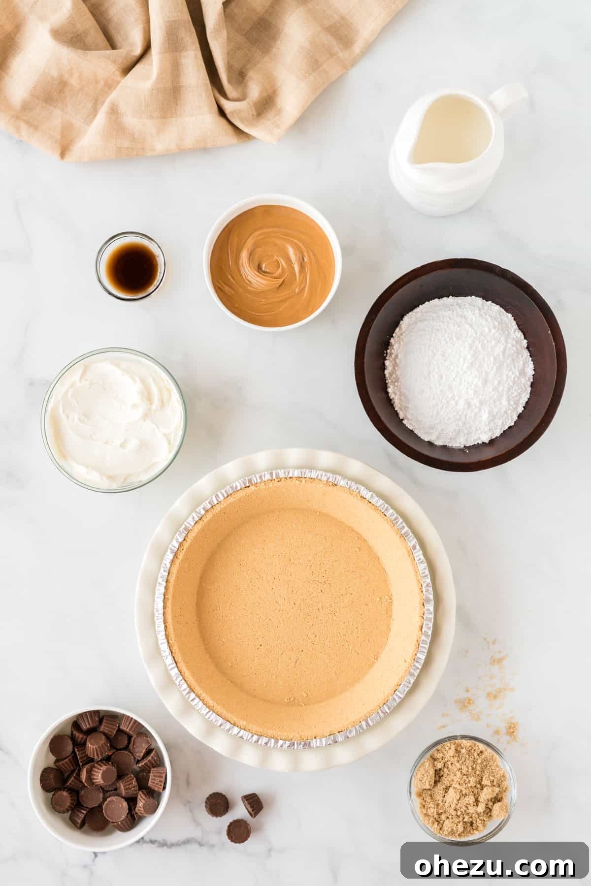 All the essential ingredients for making the no bake peanut butter pie laid out neatly on a kitchen counter, including peanut butter, cream cheese, heavy cream, sugars, and a graham cracker crust.