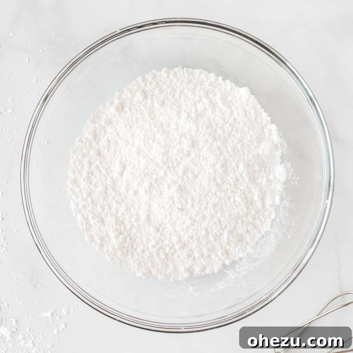 Close-up of powdered sugar being measured into a mixing bowl, an initial step for making homemade whipped cream from scratch.