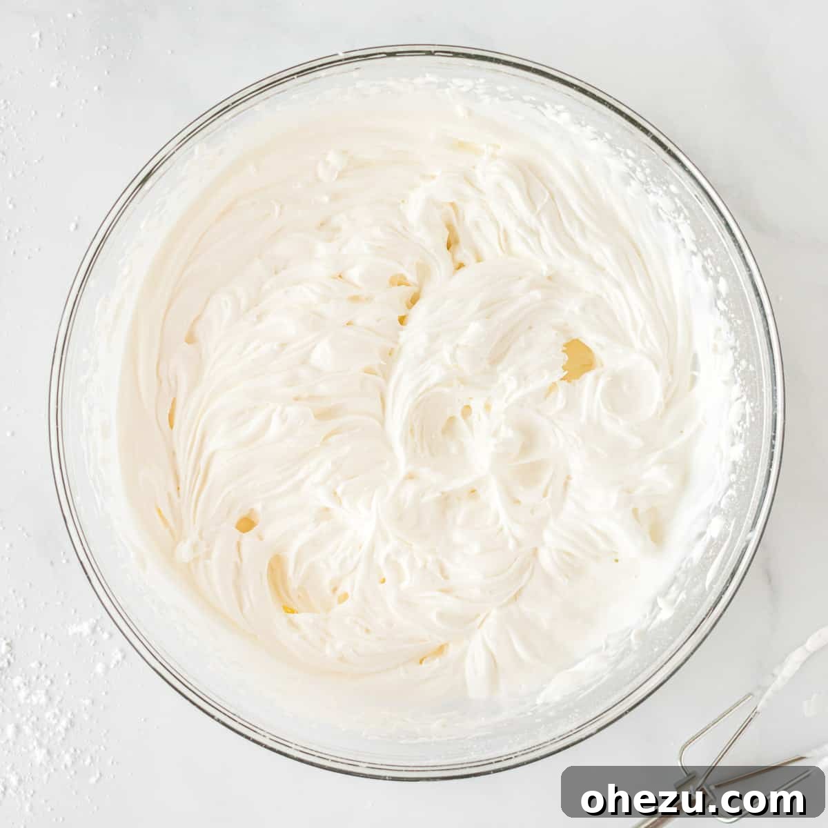 Freshly whipped homemade cream with stiff peaks shown in a clear glass bowl, perfectly prepared and ready to be incorporated into the pie filling.