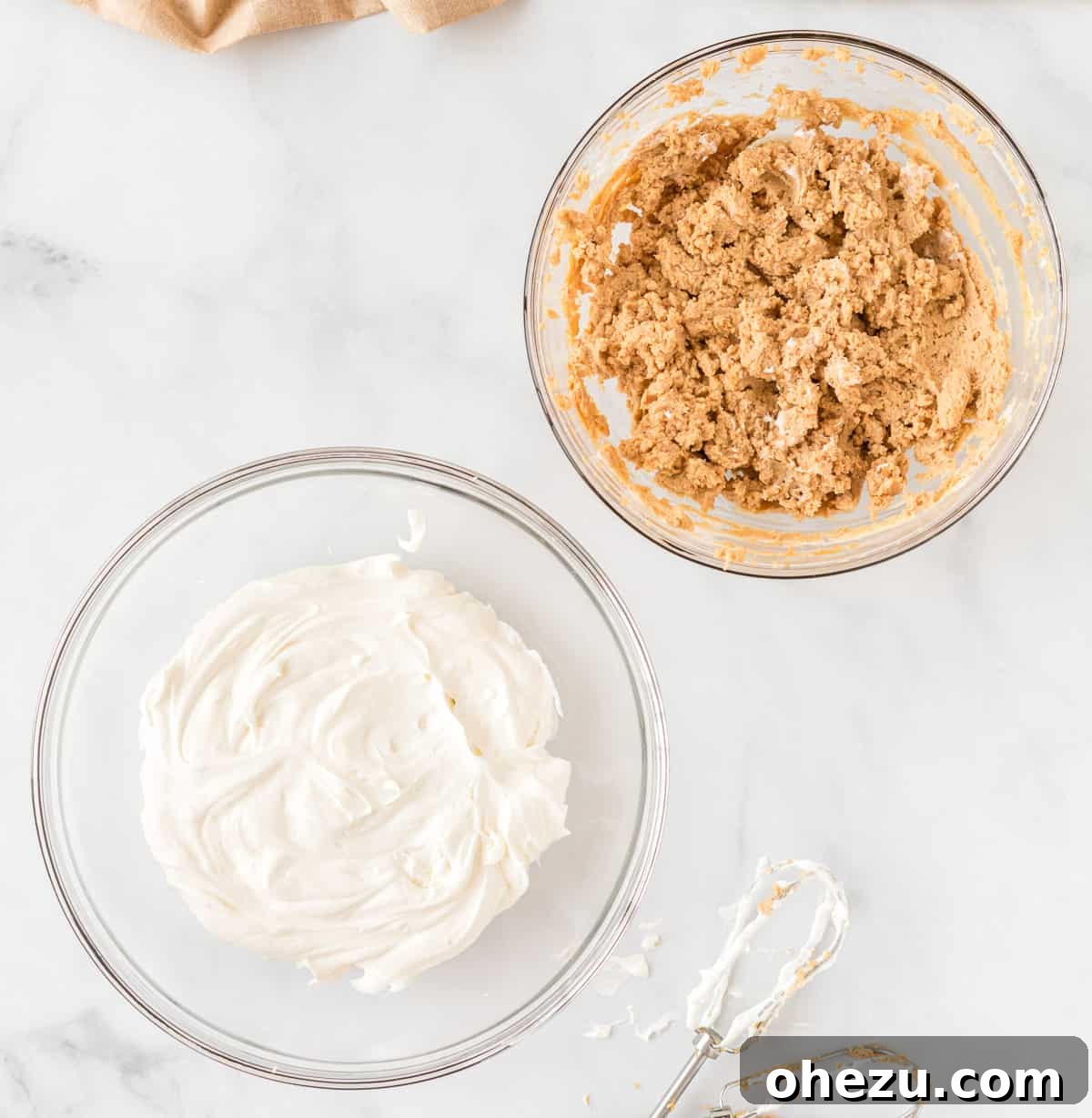 Two separate bowls on a counter, one containing the fluffy whipped cream and the other holding the thick peanut butter cream cheese filling, just before they are mixed.