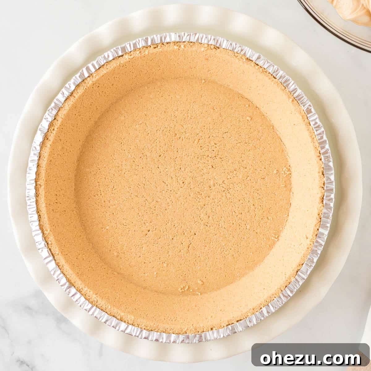 An empty, golden-brown graham cracker crust sitting neatly in a pie dish, patiently waiting to be filled with the creamy peanut butter mixture.