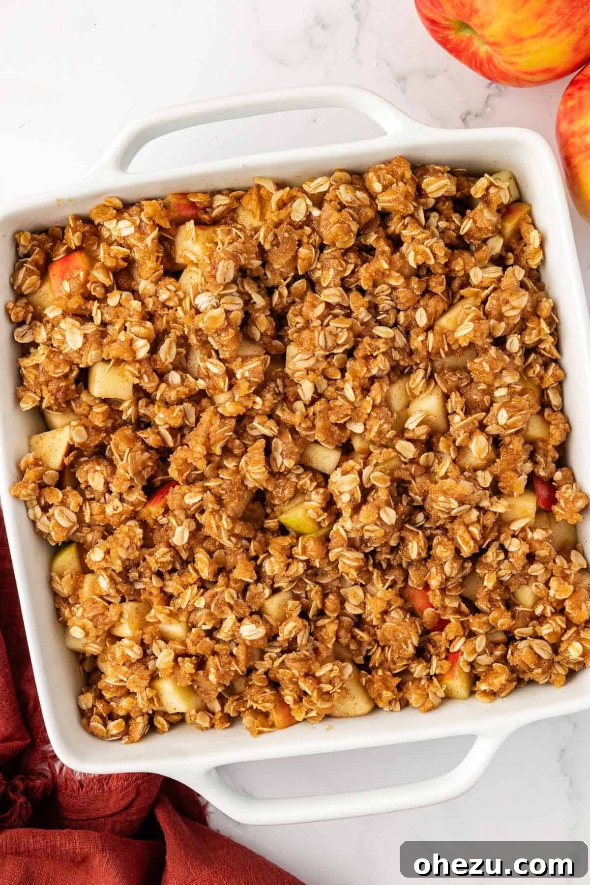 Vegan apple crisp with the topping evenly distributed over the apple filling in a baking dish, ready for the oven.