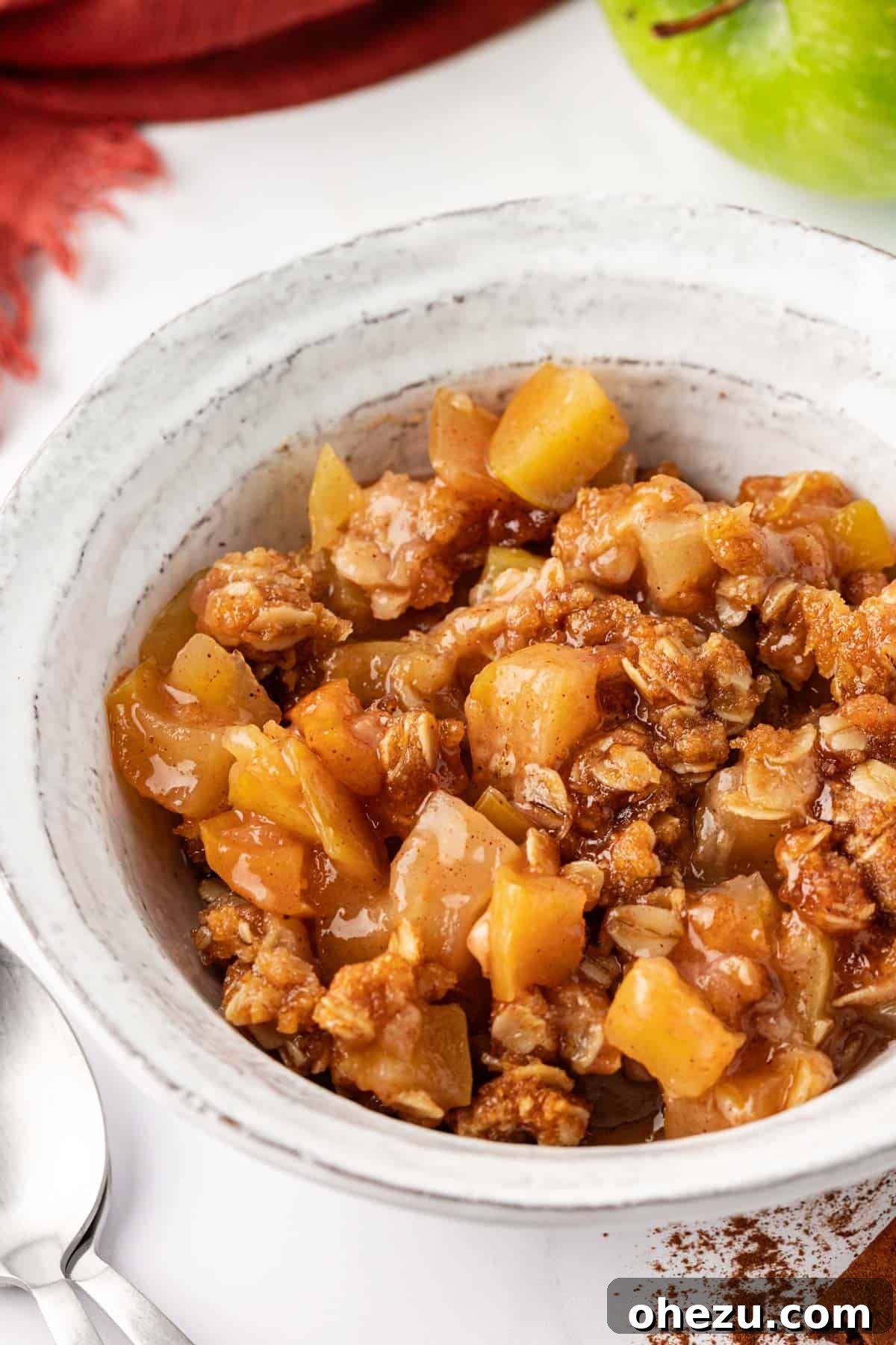A close-up of a serving of warm vegan apple crisp with a scoop of vegan vanilla ice cream melting on top, garnished slightly.