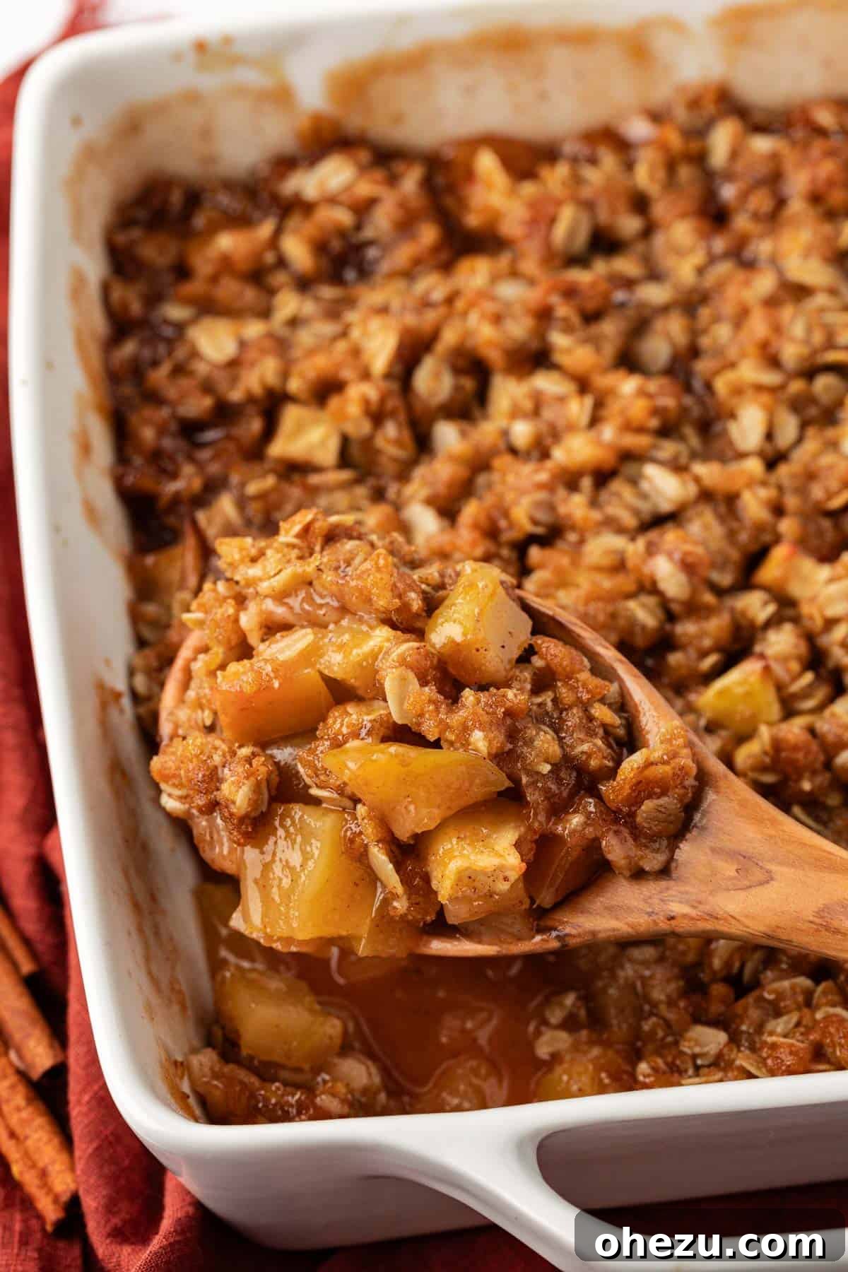 A close-up of a wooden spoon digging into a freshly baked vegan apple crisp, showing the warm, gooey apple filling.