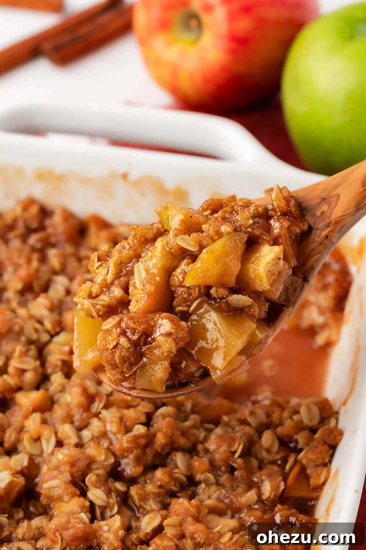 A wooden spoon scooping a generous portion of warm vegan apple crisp from a baking dish, highlighting its bubbly filling and crispy topping.