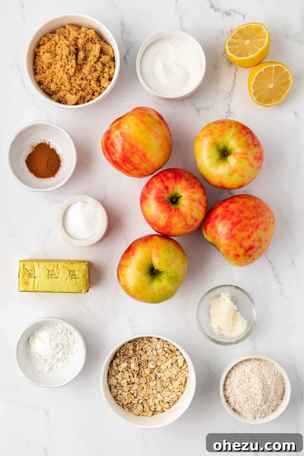 A neatly arranged flat lay of all the vegan apple crisp ingredients including apples, lemon, sugars, spices, flour, oats, coconut oil, and vegan butter.