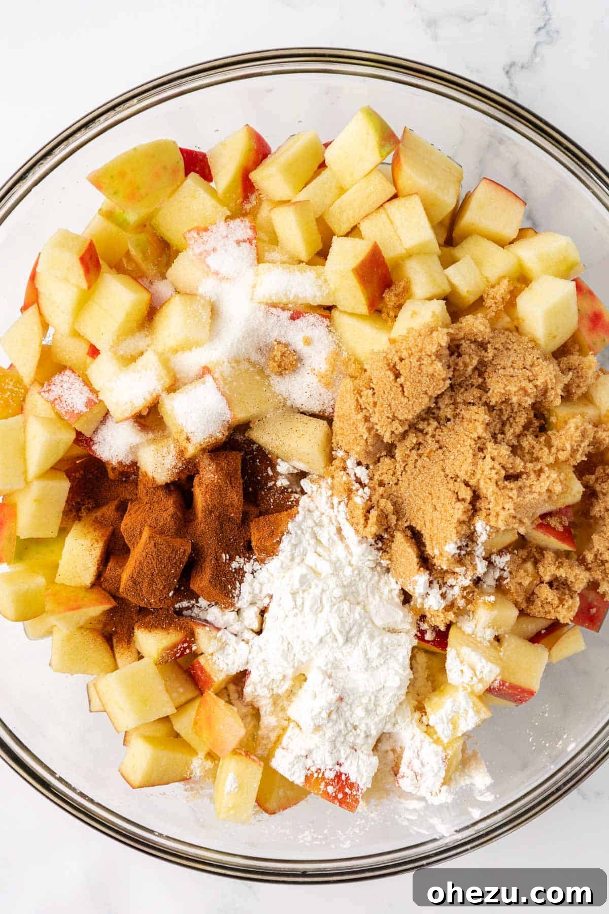 Adding cinnamon and other spices to the diced apples in a mixing bowl for the filling.