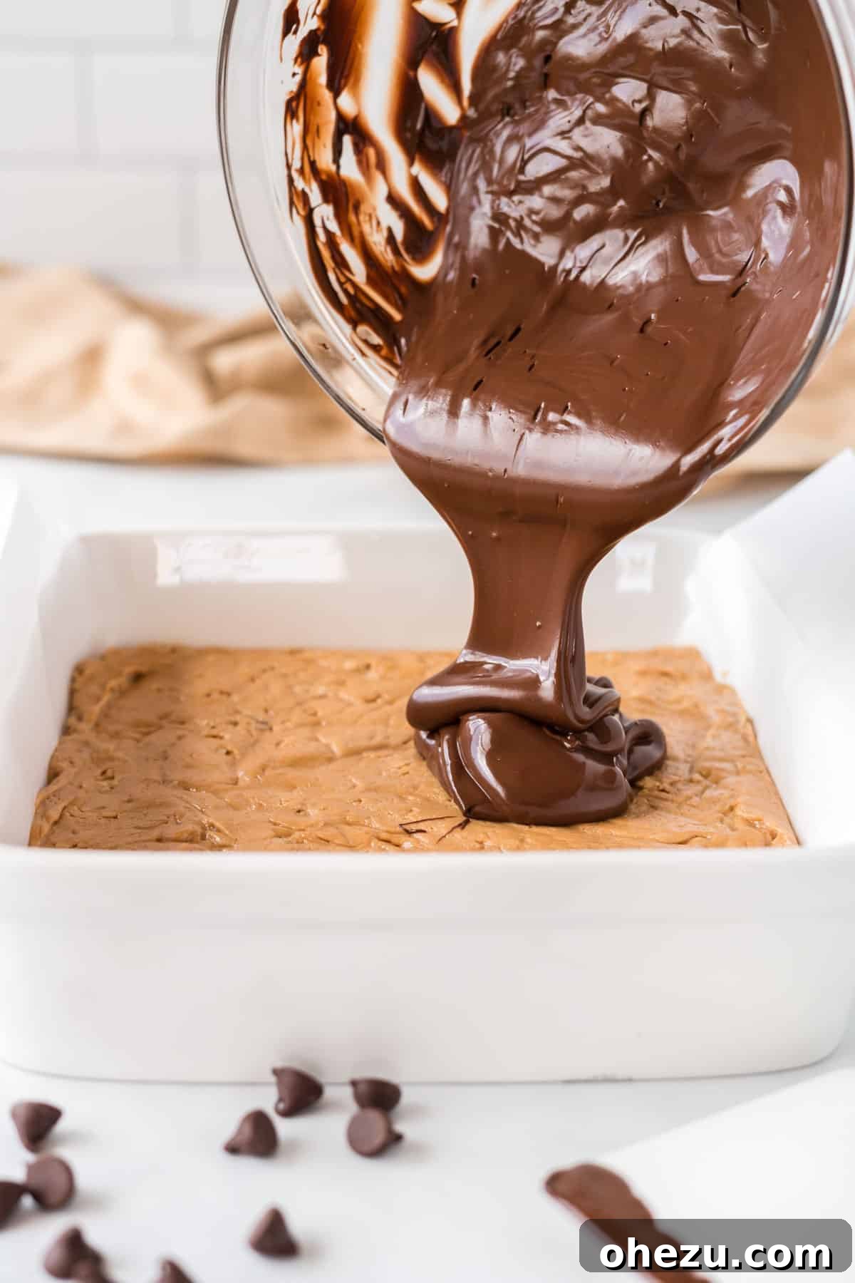 Pouring the melted chocolate over the peanut butter protein bar base