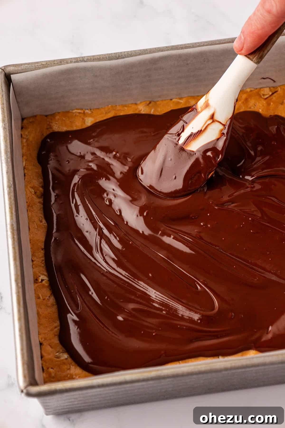 Spreading the melted chocolate evenly over the protein bars with a spatula