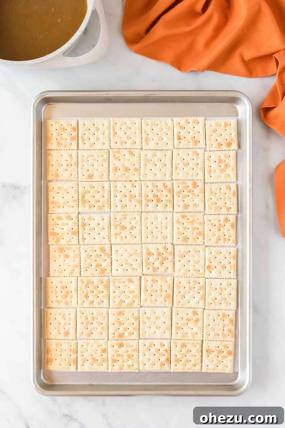 A baking sheet neatly lined with rows of saltine crackers, preparing for the toffee layer.