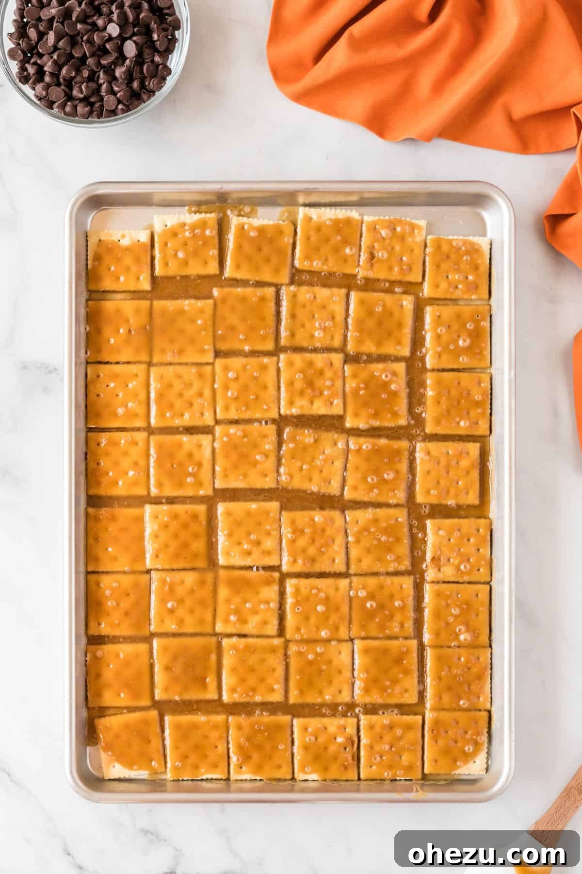 Saltine crackers completely covered in a rich, golden toffee layer on a baking sheet, freshly baked and bubbling.