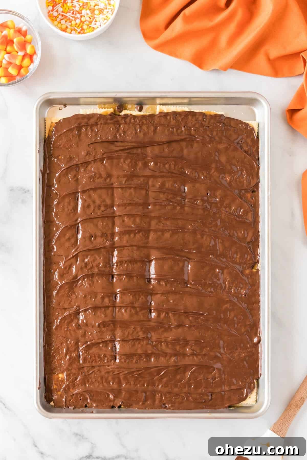 Melted chocolate smoothly spread over the Halloween crack base on the sheet pan, creating a uniform layer.