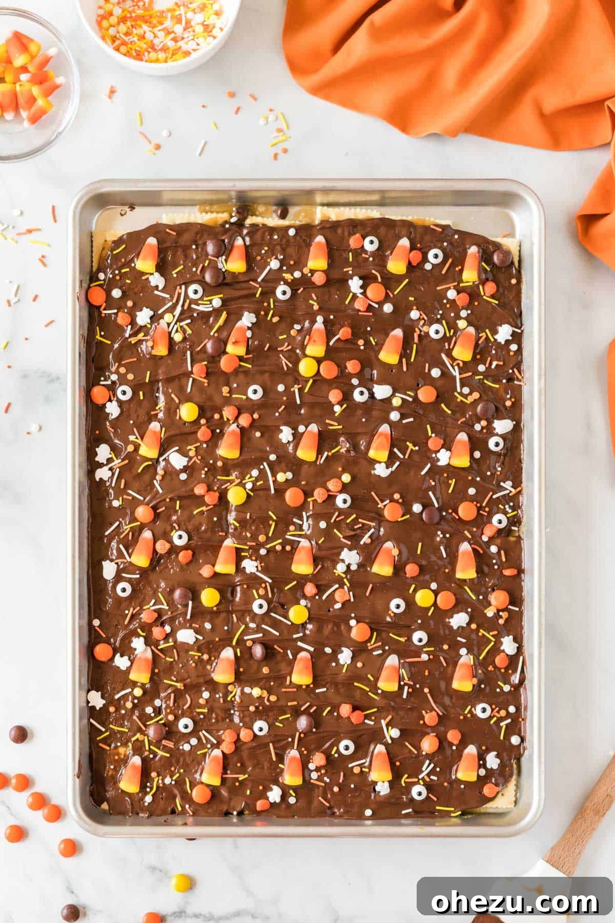 The Halloween crack candy base generously decorated with colorful Halloween candies, eye candies, Reese's Pieces, and candy corn on the still-soft melted chocolate layer.