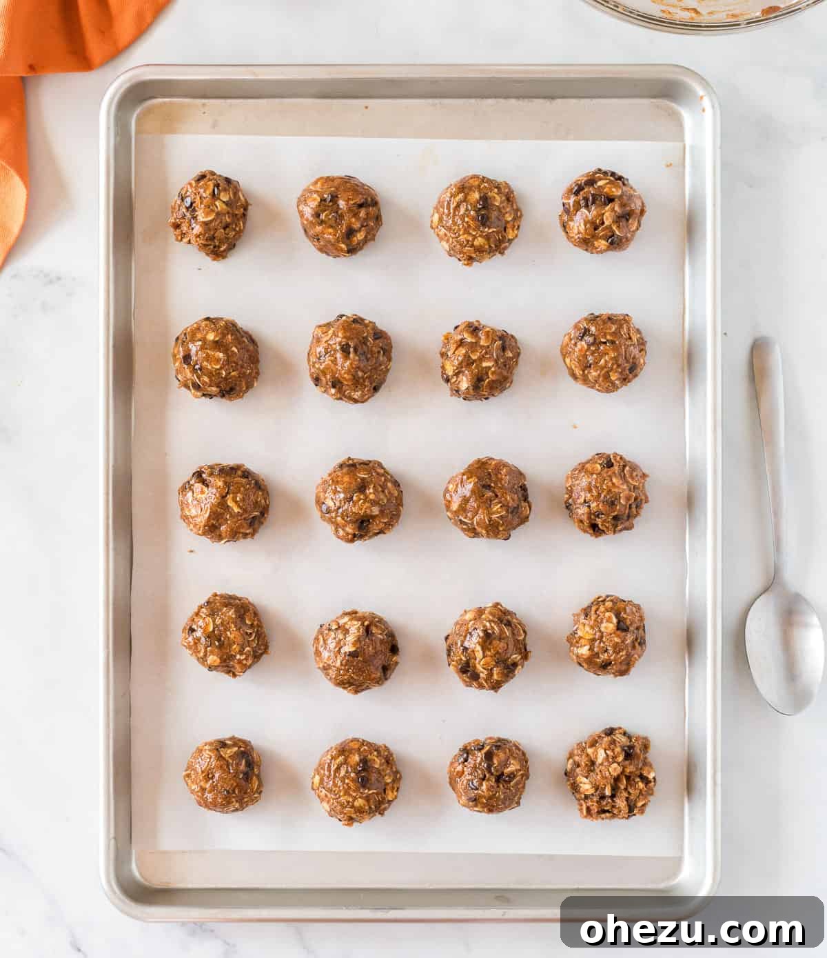 Rows of pumpkin protein balls neatly lined up on a baking sheet, freshly made and ready to be chilled.