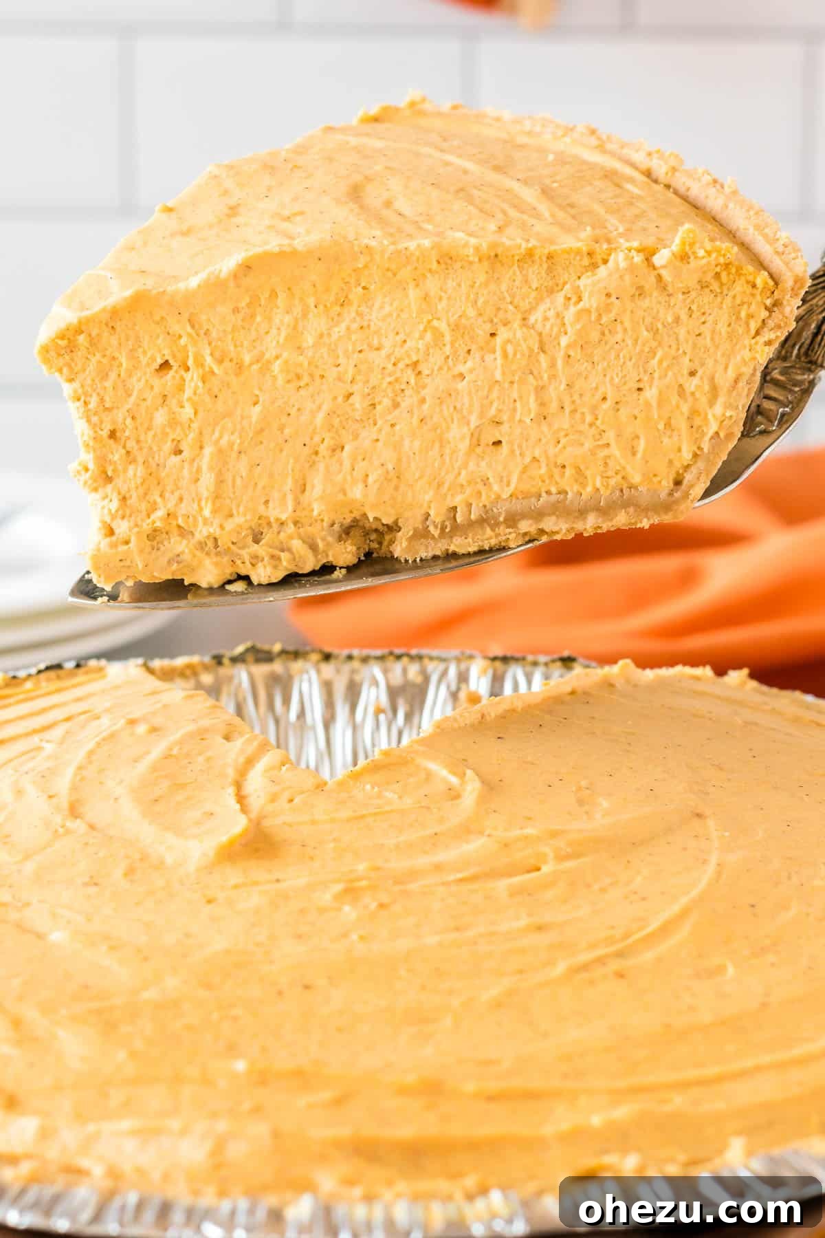 Velvet Pumpkin Pie 2 A beautiful slice of Pumpkin Cream Pie being taken from the pie dish, showcasing its fluffy whipped topping and smooth pumpkin filling.
