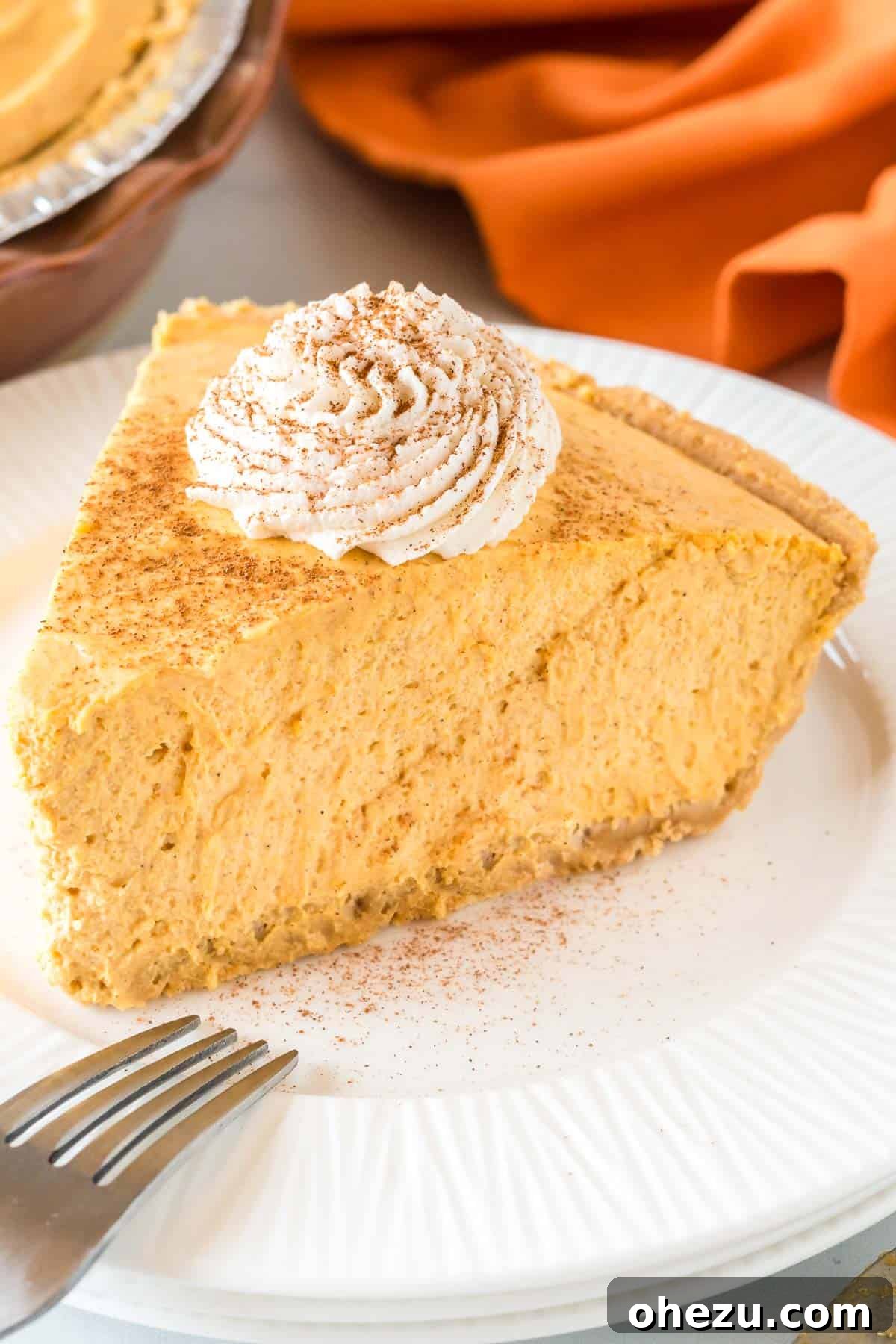 Velvet Pumpkin Pie 3 Close-up of a perfectly sliced pumpkin cream pie, topped with a swirl of whipped cream and a sprinkle of cinnamon.