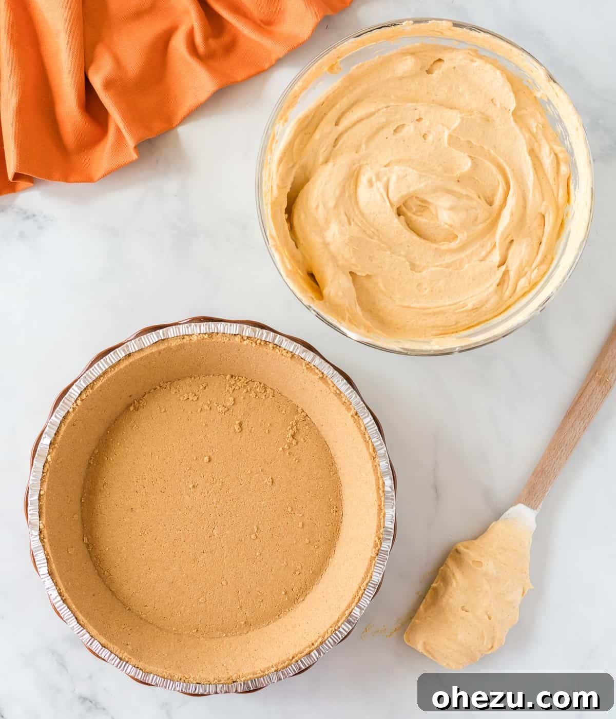 Velvet Pumpkin Pie 10 The creamy pumpkin filling being scooped into a graham cracker pie crust, ready for spreading.