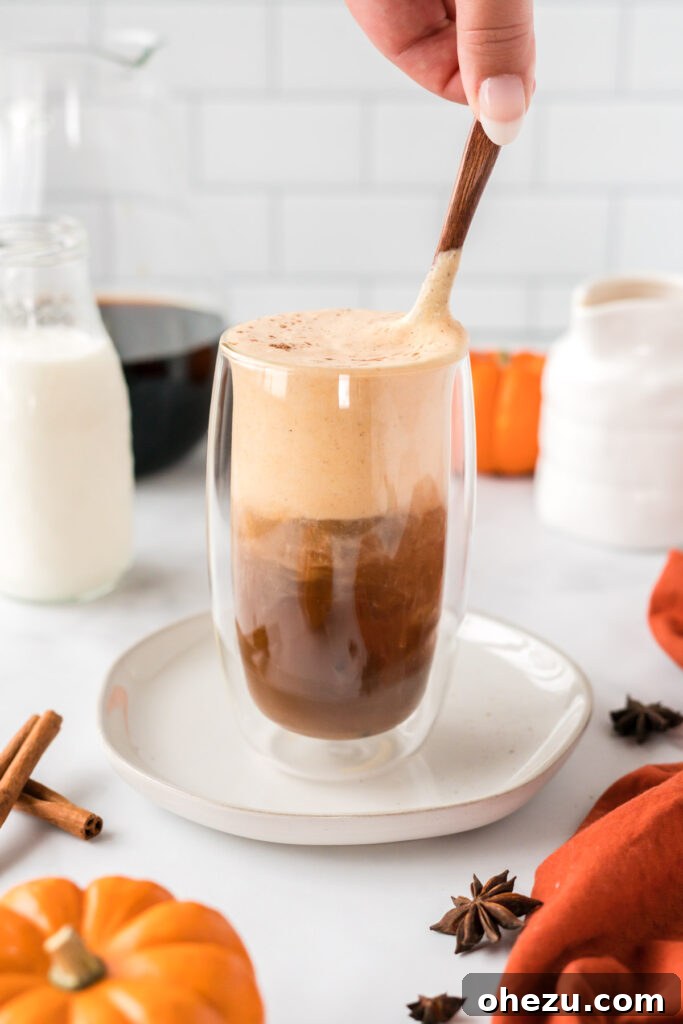 Spiced Pumpkin Cold Brew 10 A spoon gently stirring the pumpkin cream into the cold brew coffee, blending the layers into a harmonious, creamy beverage.