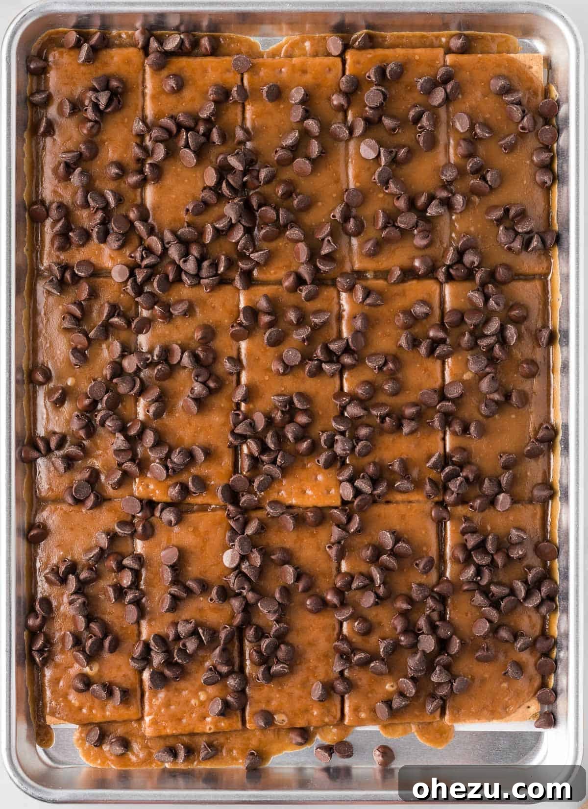A generous scattering of semi-sweet chocolate chips distributed evenly over the warm toffee and graham cracker base, beginning to glisten as they melt.