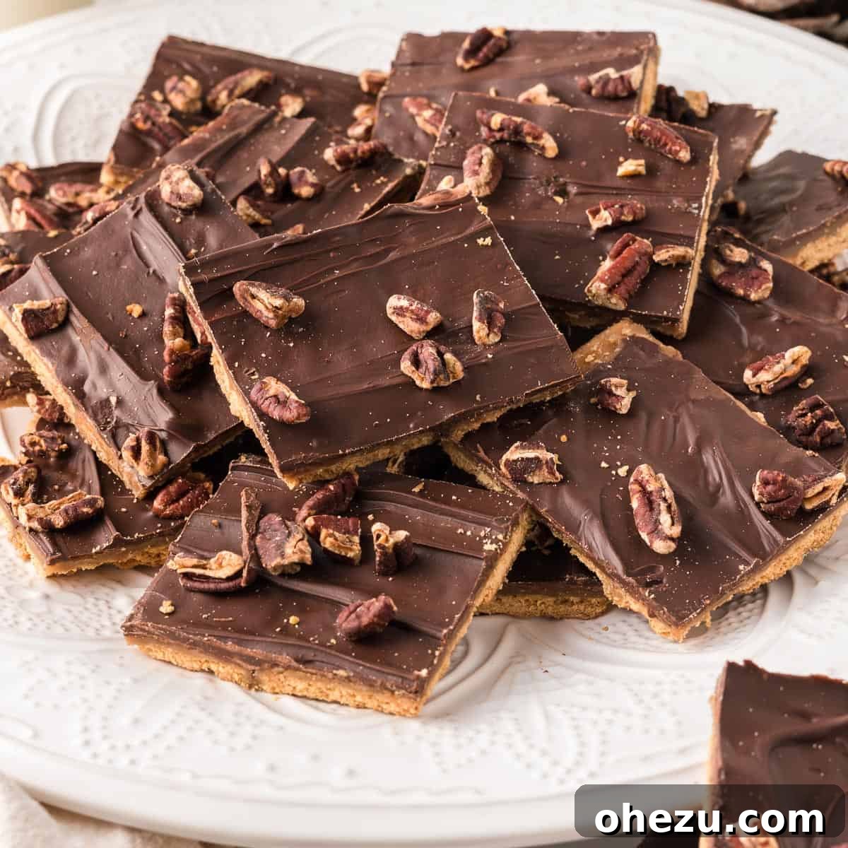 A charming white plate filled with individual squares of homemade graham cracker toffee, meticulously cut and ready to be savored.