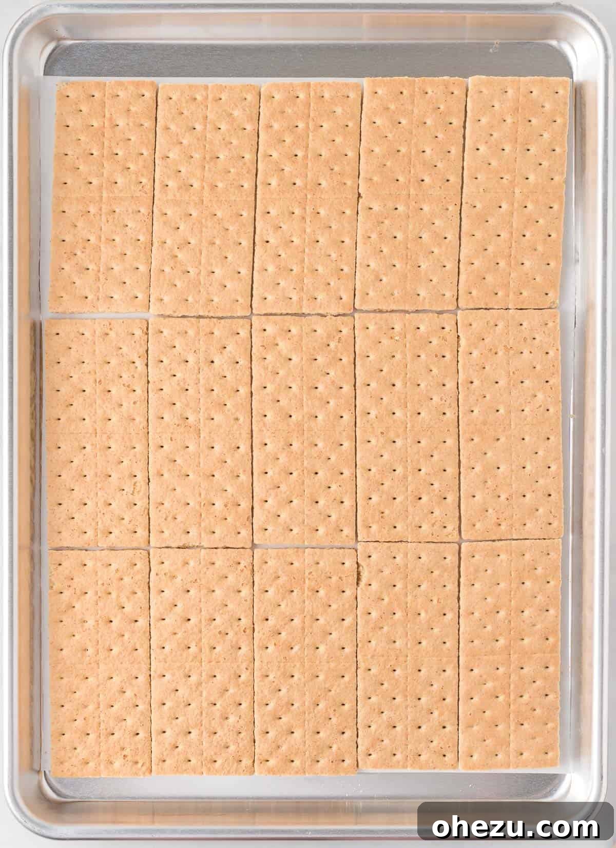 Graham cracker sheets perfectly aligned in neat rows on a parchment-lined baking sheet, meticulously forming the sturdy base for the upcoming toffee layers.