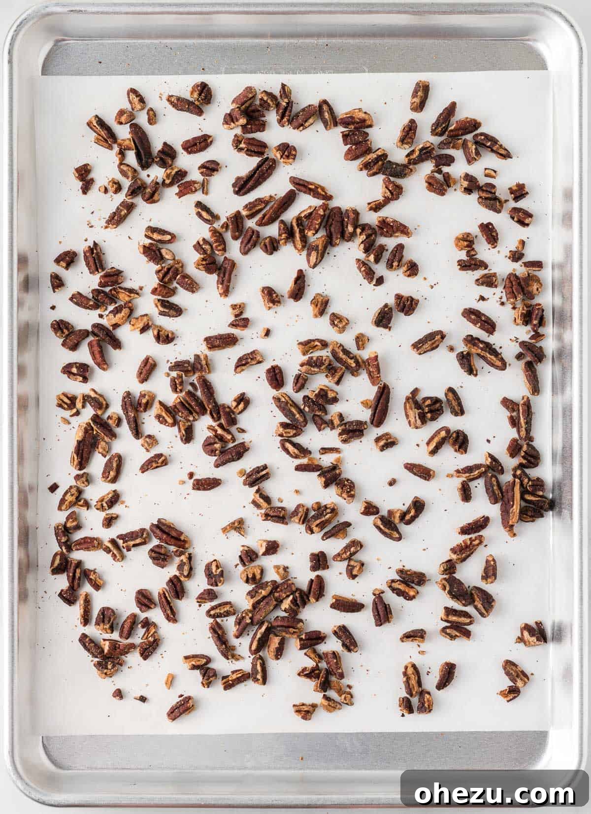 Toasted pecan pieces evenly spread on a small baking sheet, their rich color and aroma enhanced by the oven's heat, ready to be incorporated.