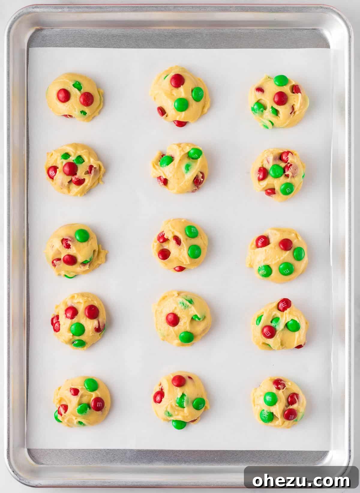 Holiday Cookie Magic from a Box 9 Scooped portions of cake mix Christmas cookie dough on a parchment-lined baking sheet, topped with extra M&M's before baking.