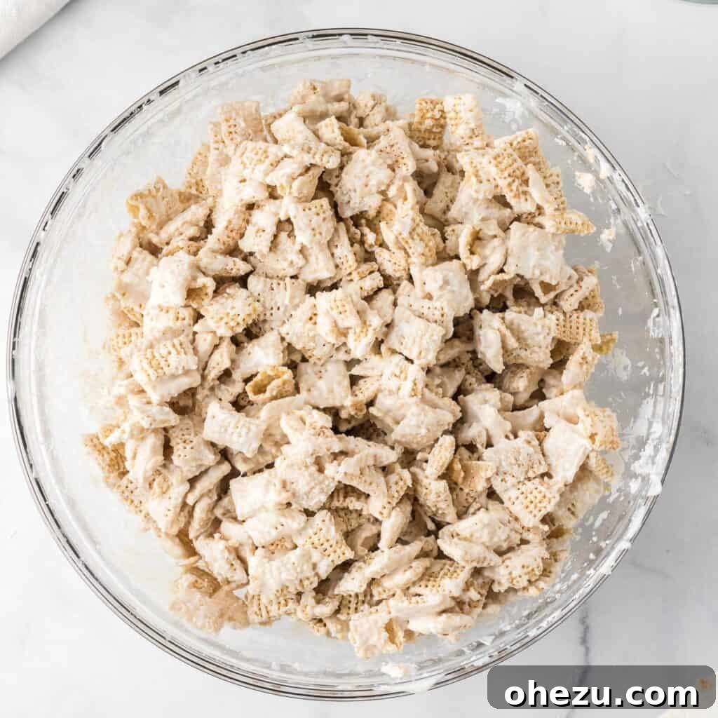 Cookies and Cream Puppy Chow 11 Rice Chex cereal coated evenly in melted white chocolate in a mixing bowl.