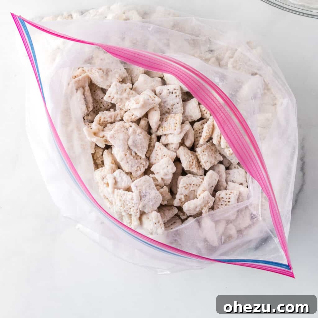 Cookies and Cream Puppy Chow 12 White chocolate muddy buddies shaking inside a ziploc bag with Oreo crumbs and powdered sugar.