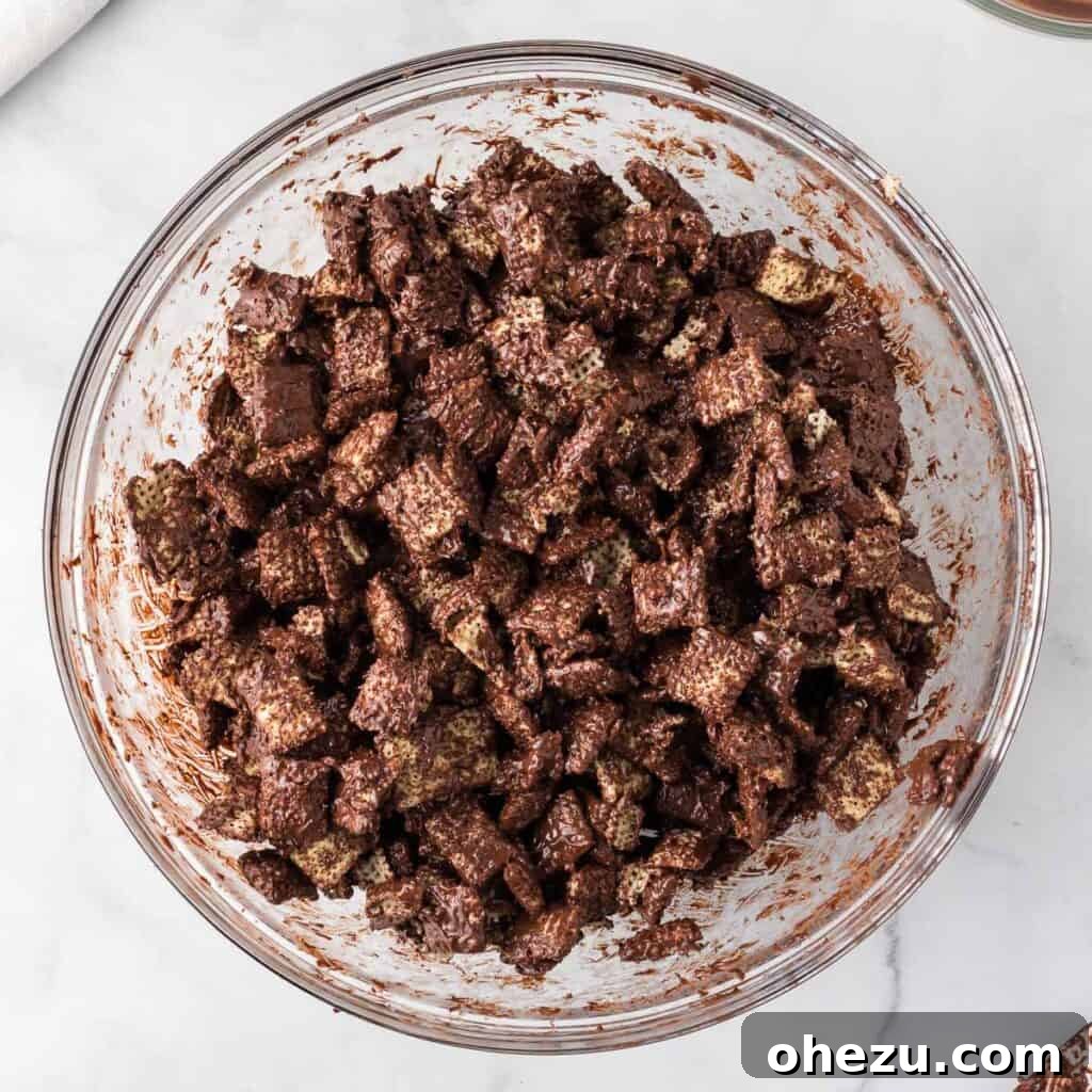 Cookies and Cream Puppy Chow 9 Rice Chex cereal being gently stirred in a bowl after being coated with melted semi-sweet chocolate.