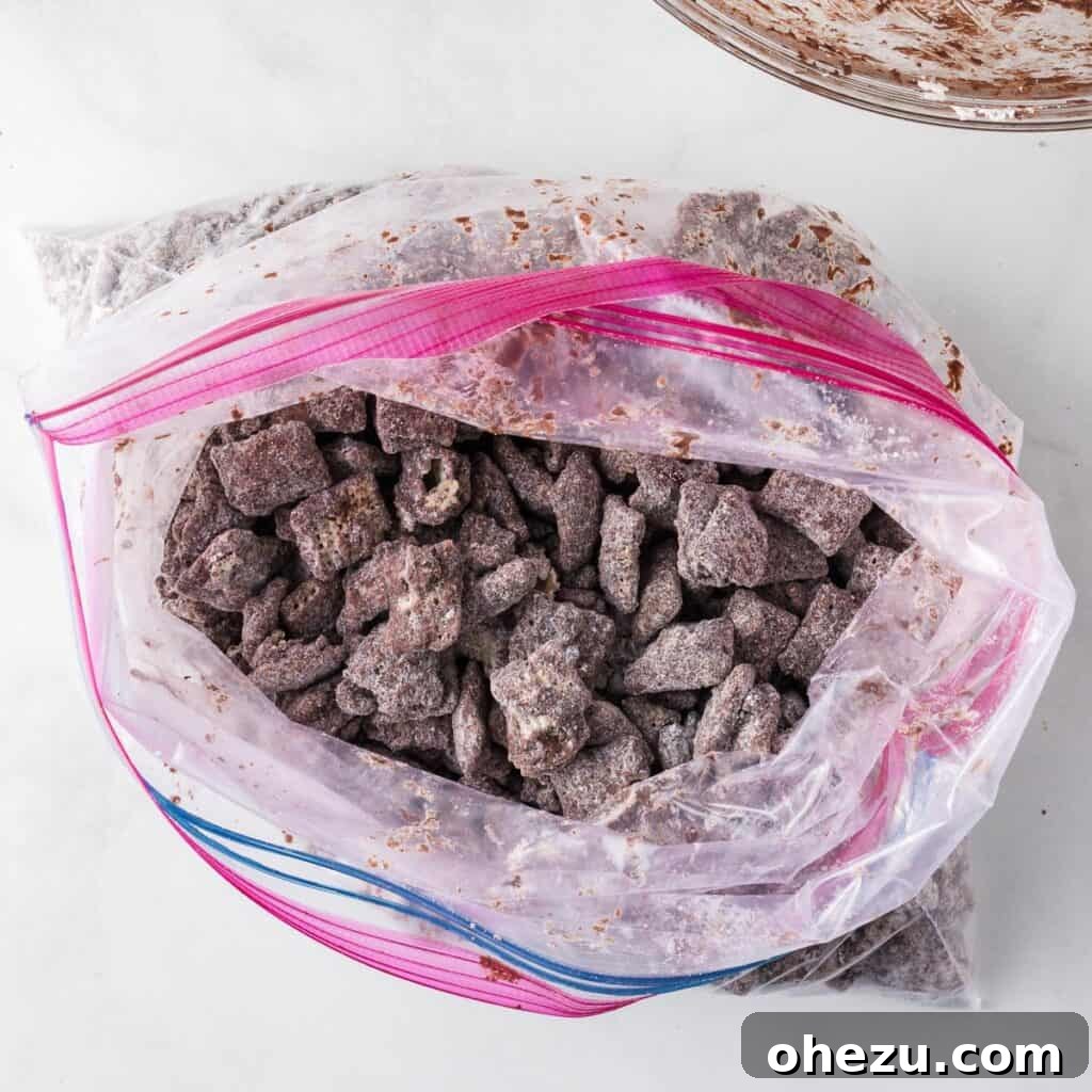 Cookies and Cream Puppy Chow 10 Semi-sweet chocolate muddy buddies shaking inside a ziploc bag with Oreo crumbs and powdered sugar.