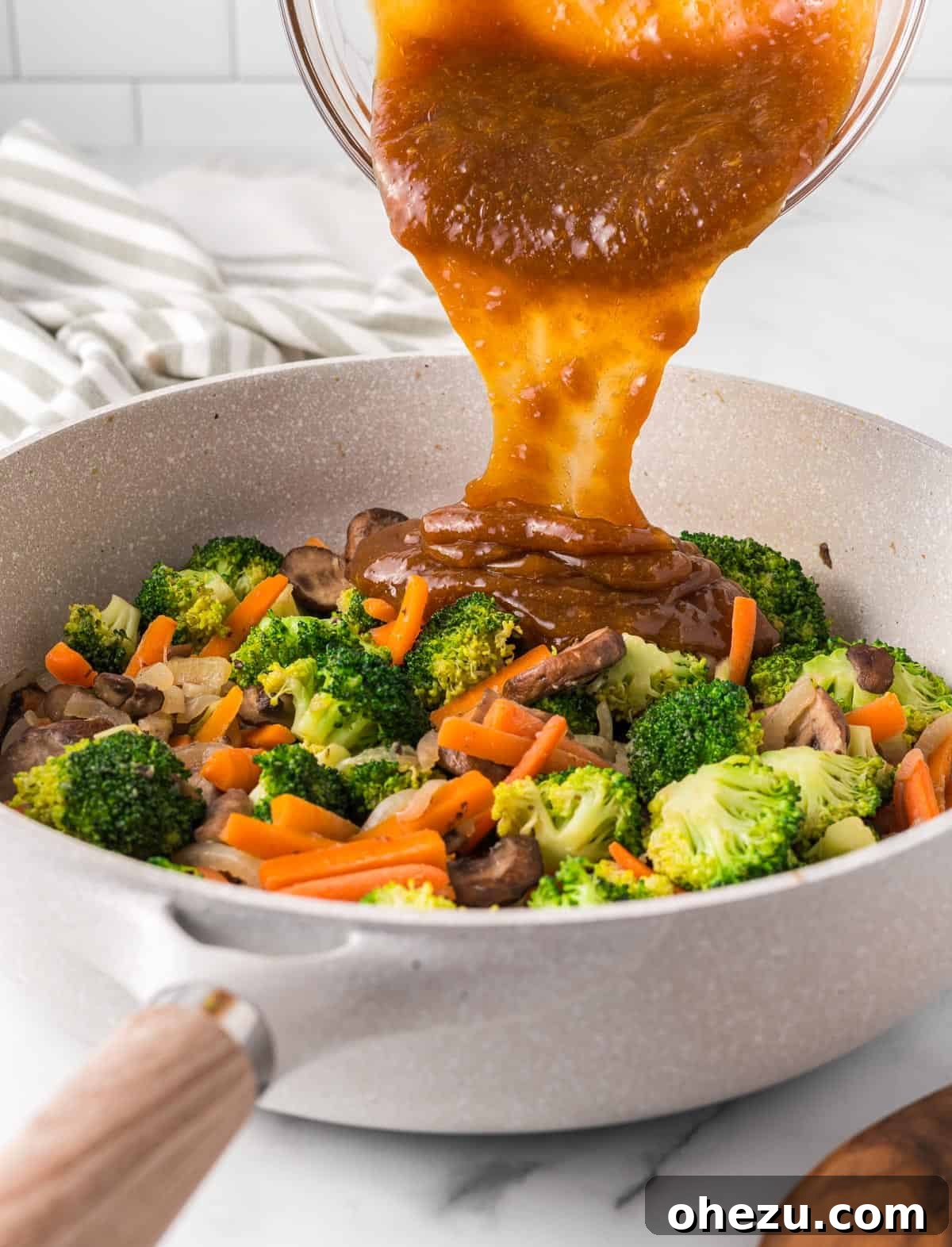 A close-up shot capturing the moment luscious teriyaki sauce is poured over the medley of colorful, cooked vegetables in a hot skillet, creating an appealing sheen.