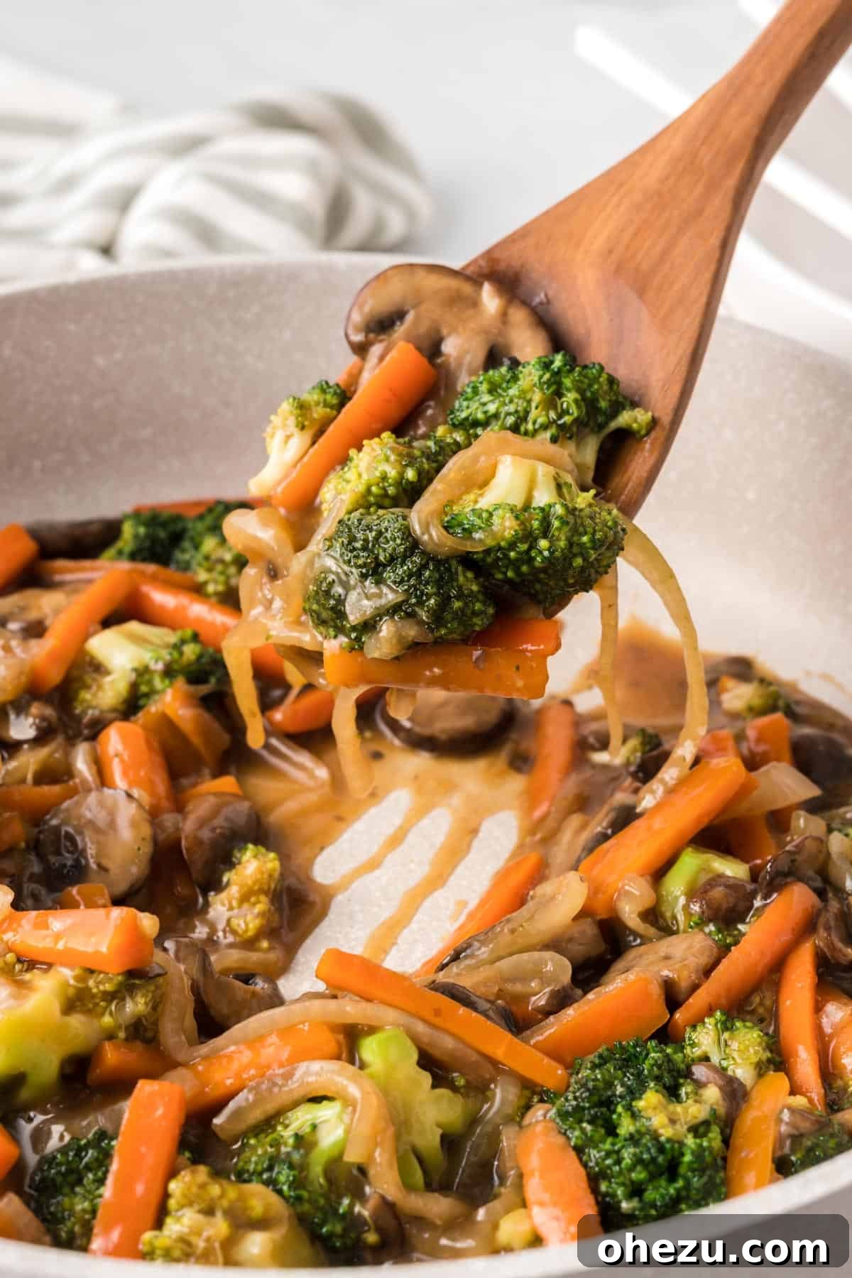 A wooden spoon delicately scooping a generous portion of vibrant teriyaki vegetables from a hot skillet, ready to be served into a bowl.