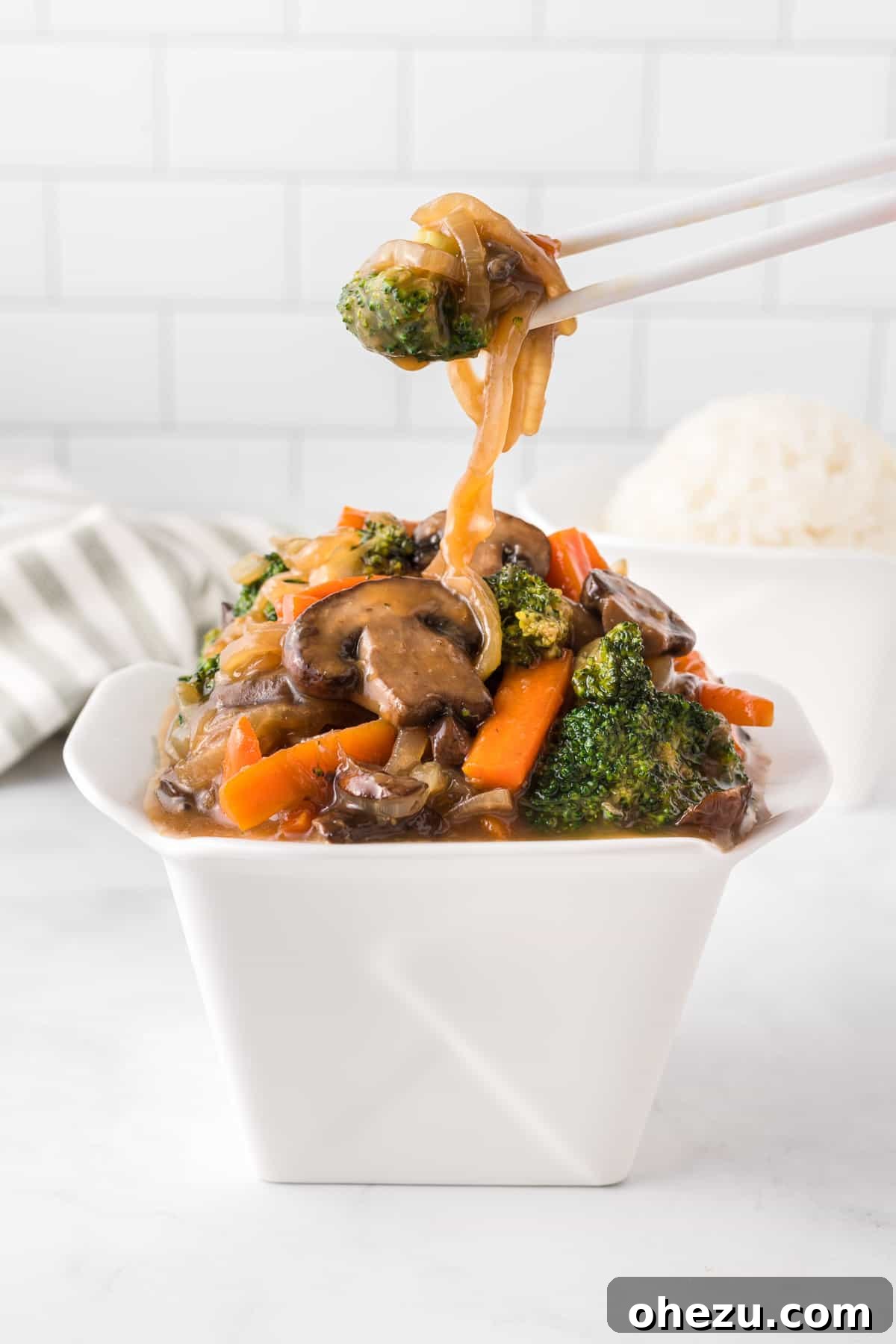 Chopsticks expertly picking up glossy teriyaki vegetables from a classic Asian takeout container, tempting for a quick bite.