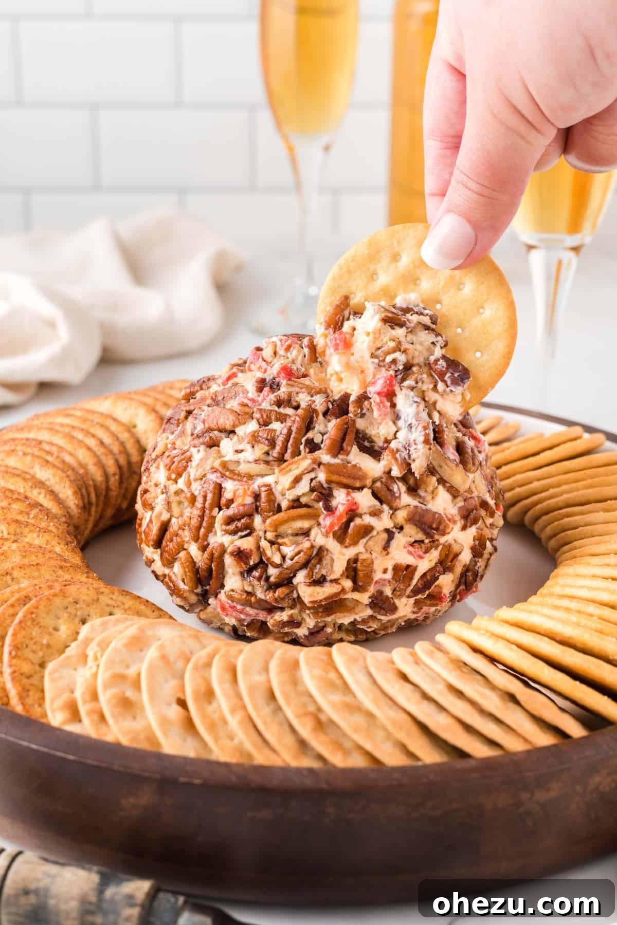 cracker dipping into a cheese ball, highlighting the creamy texture and pecan coating