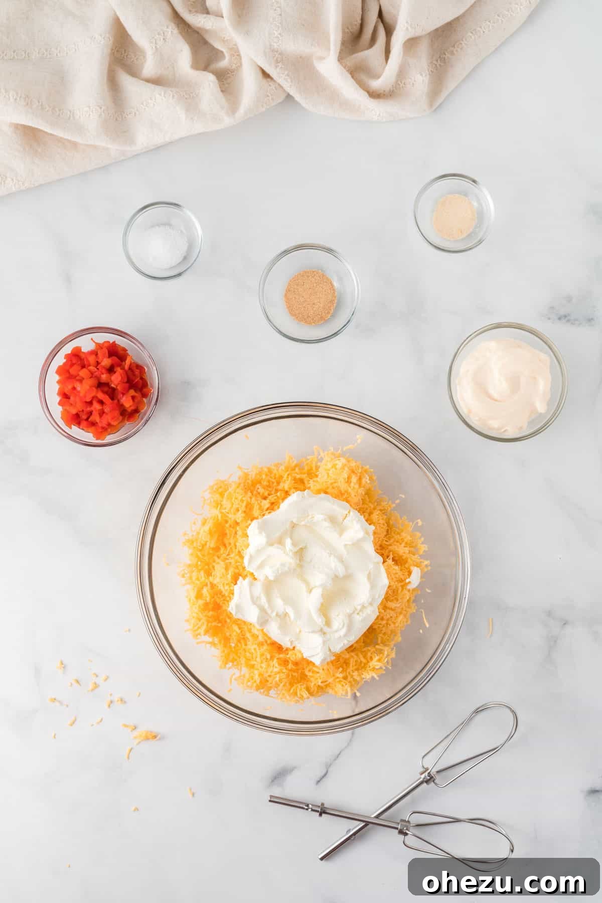 softened cream cheese and freshly grated cheddar cheese in a bowl, surrounded by other ingredients