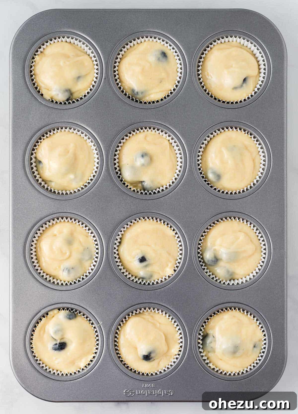 Muffin batter neatly distributed into individual muffin liners within a muffin tin, ready for topping