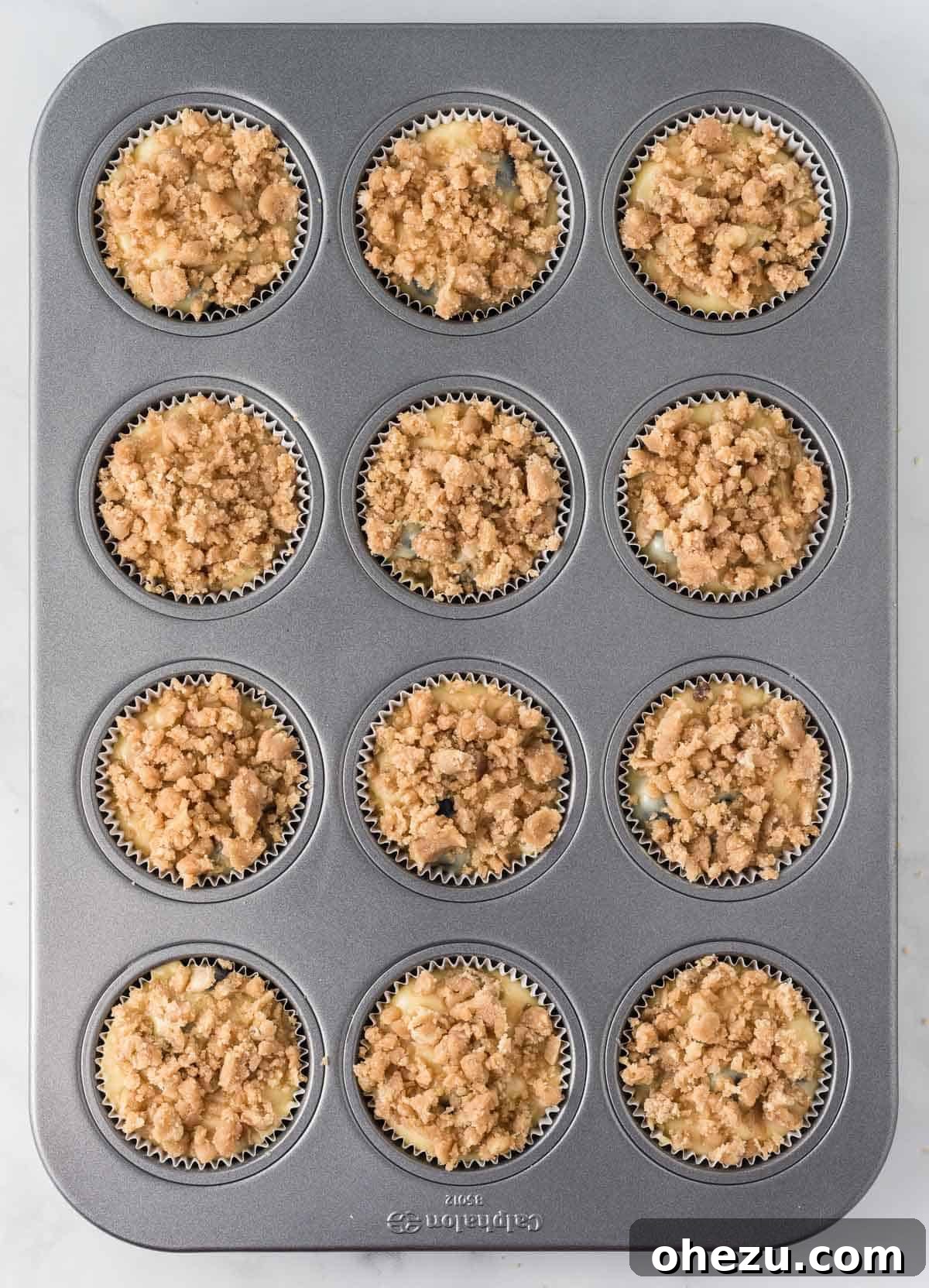 Streusel topping being generously sprinkled over the raw blueberry muffin batter in the muffin cups