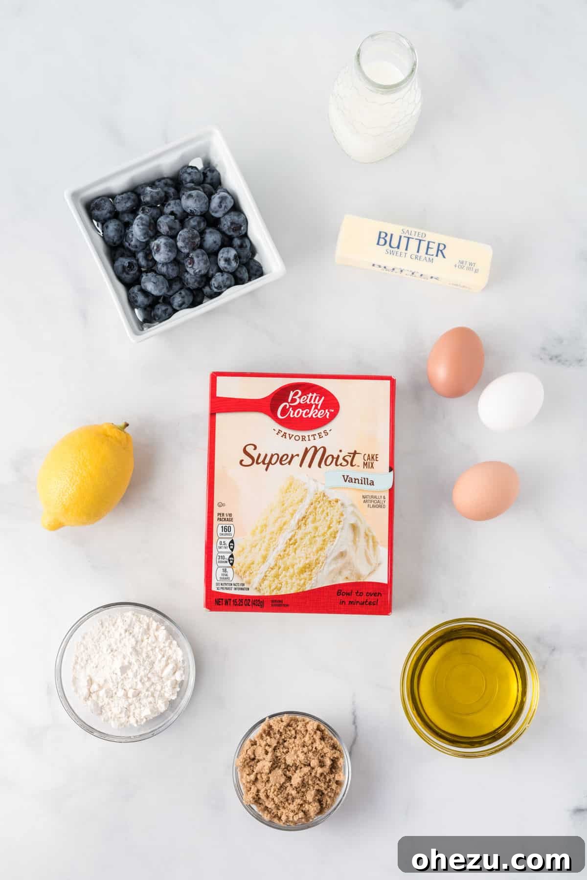 All essential ingredients laid out for making cake mix blueberry muffins, including cake mix, fresh blueberries, eggs, milk, and streusel components