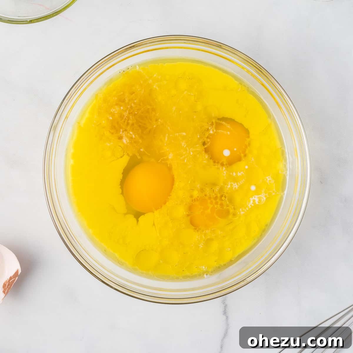 Whisked eggs, milk, lemon zest, and olive oil combined in a bowl, forming the wet ingredients for the muffin batter