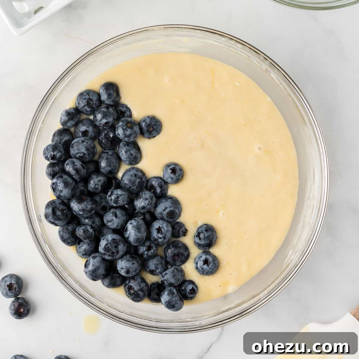 Fresh blueberries being gently folded into the prepared cake mix muffin batter with a rubber spatula