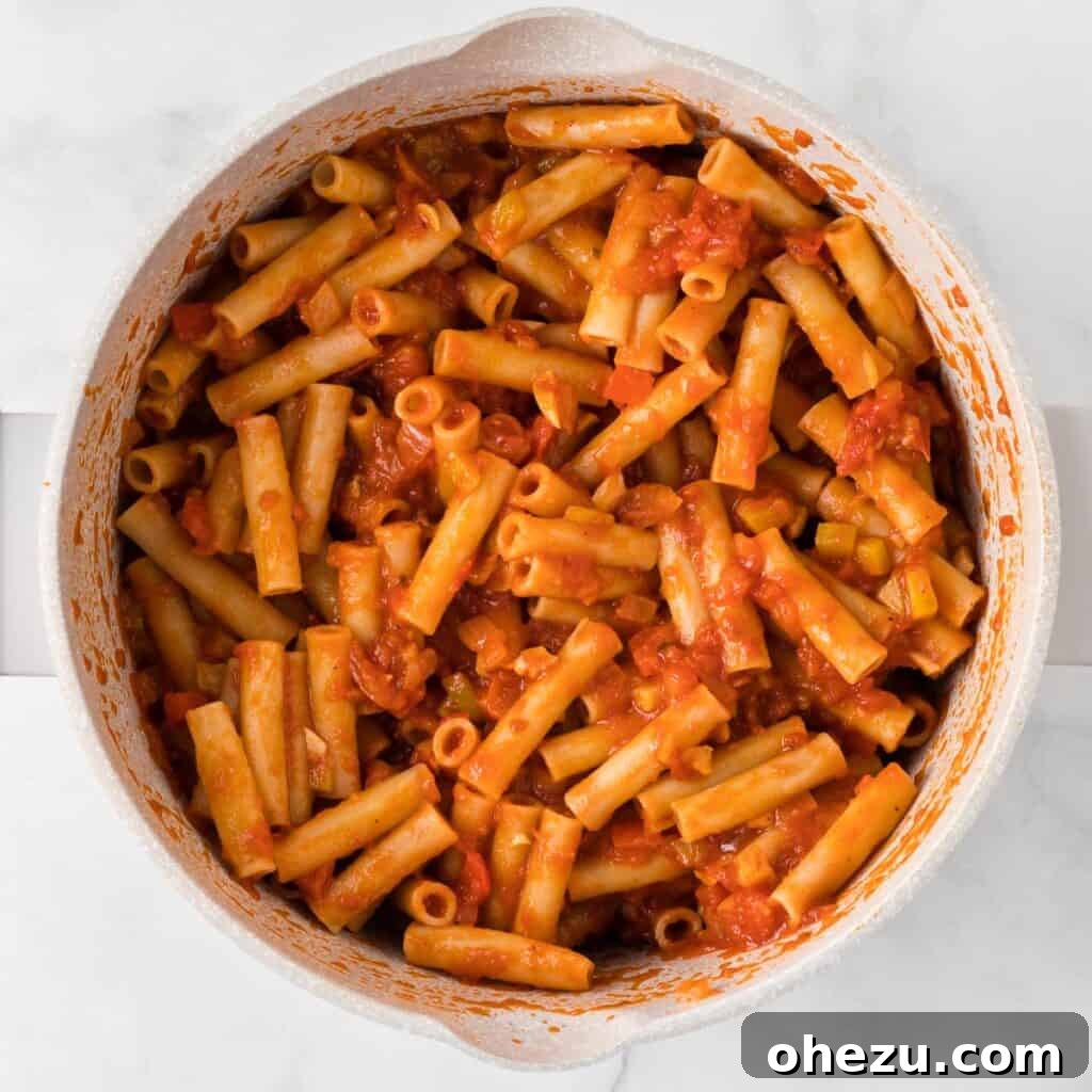 Cooked ziti pasta perfectly mixed with the rich tomato sauce and sautéed vegetables in a large pot, ready for layering.