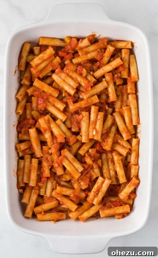 The first layer of ziti noodles and sauce evenly spread in a white casserole dish, ready for the cheese.