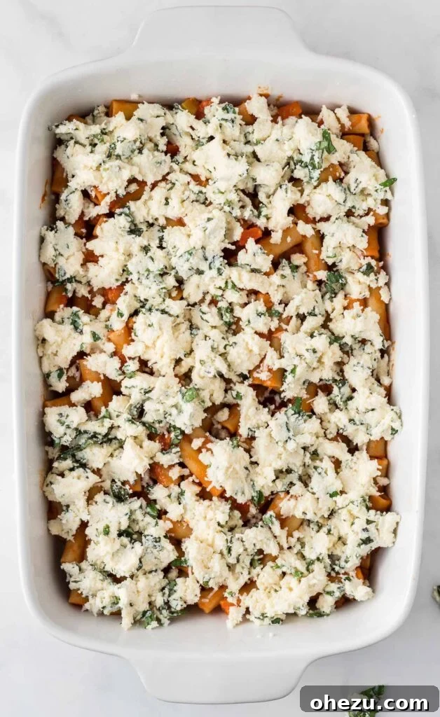 Spreading the creamy ricotta, parmesan, and basil mixture over the first layer of ziti noodles in a casserole dish.