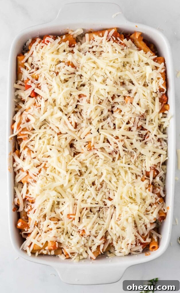 Generously topping the vegetarian baked ziti with shredded mozzarella cheese before baking, promising a bubbly, golden crust.