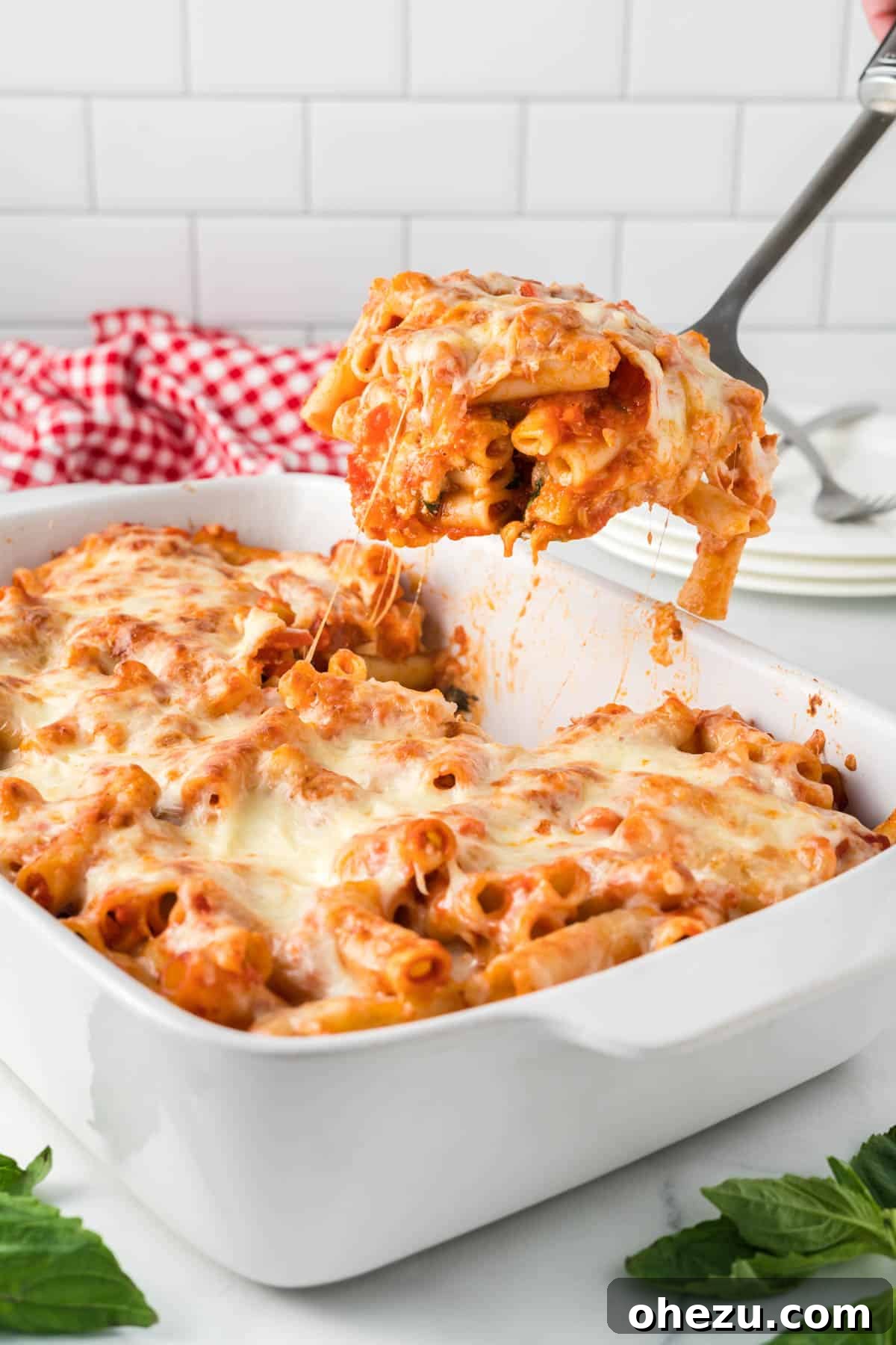 A scoop of vegetarian baked ziti being lifted from the casserole dish, showing layers of pasta, vegetables, and melted cheese, ready to serve.