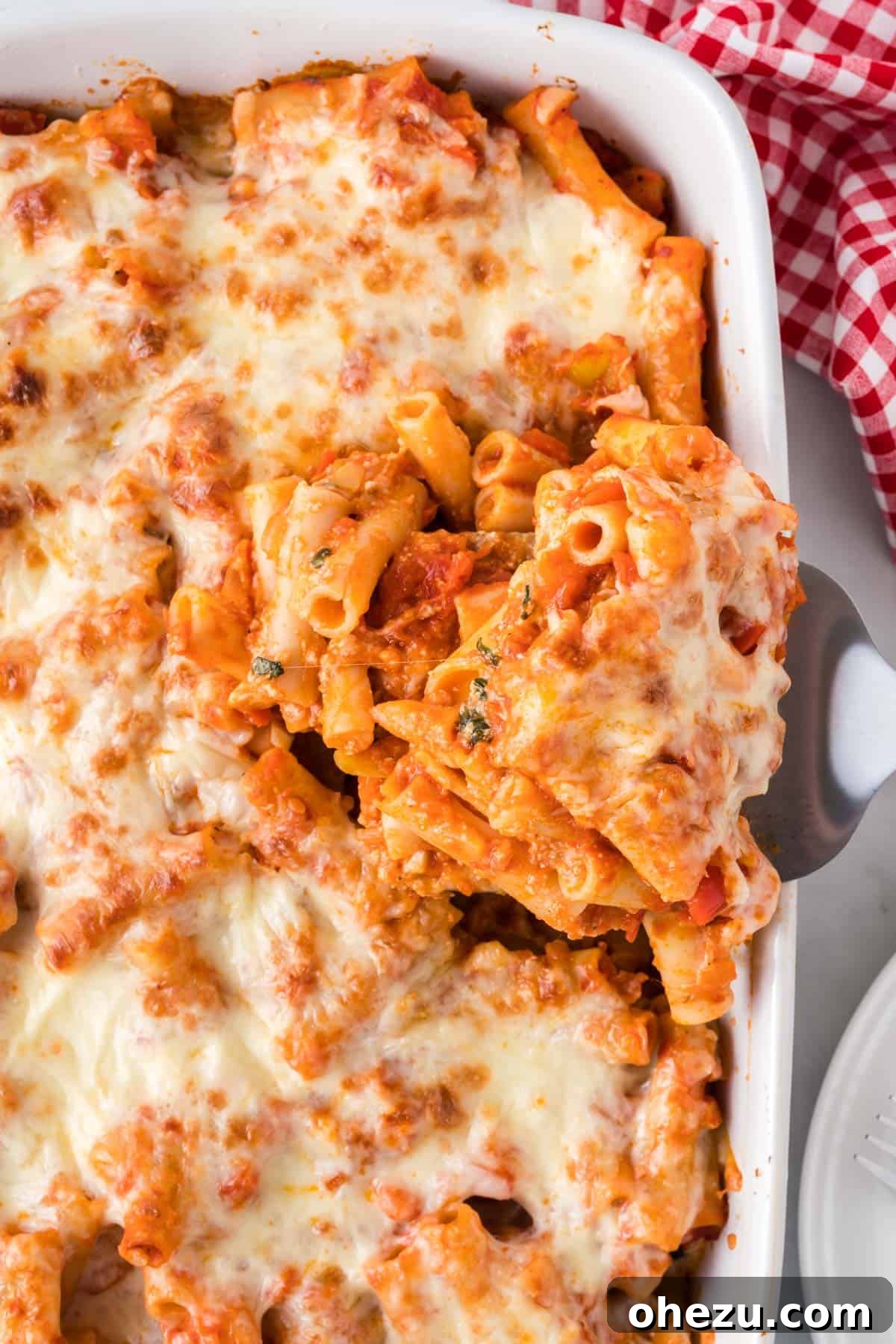 A second view of a scoop of vegetarian baked ziti being served from the casserole dish, highlighting its delicious layers and texture.