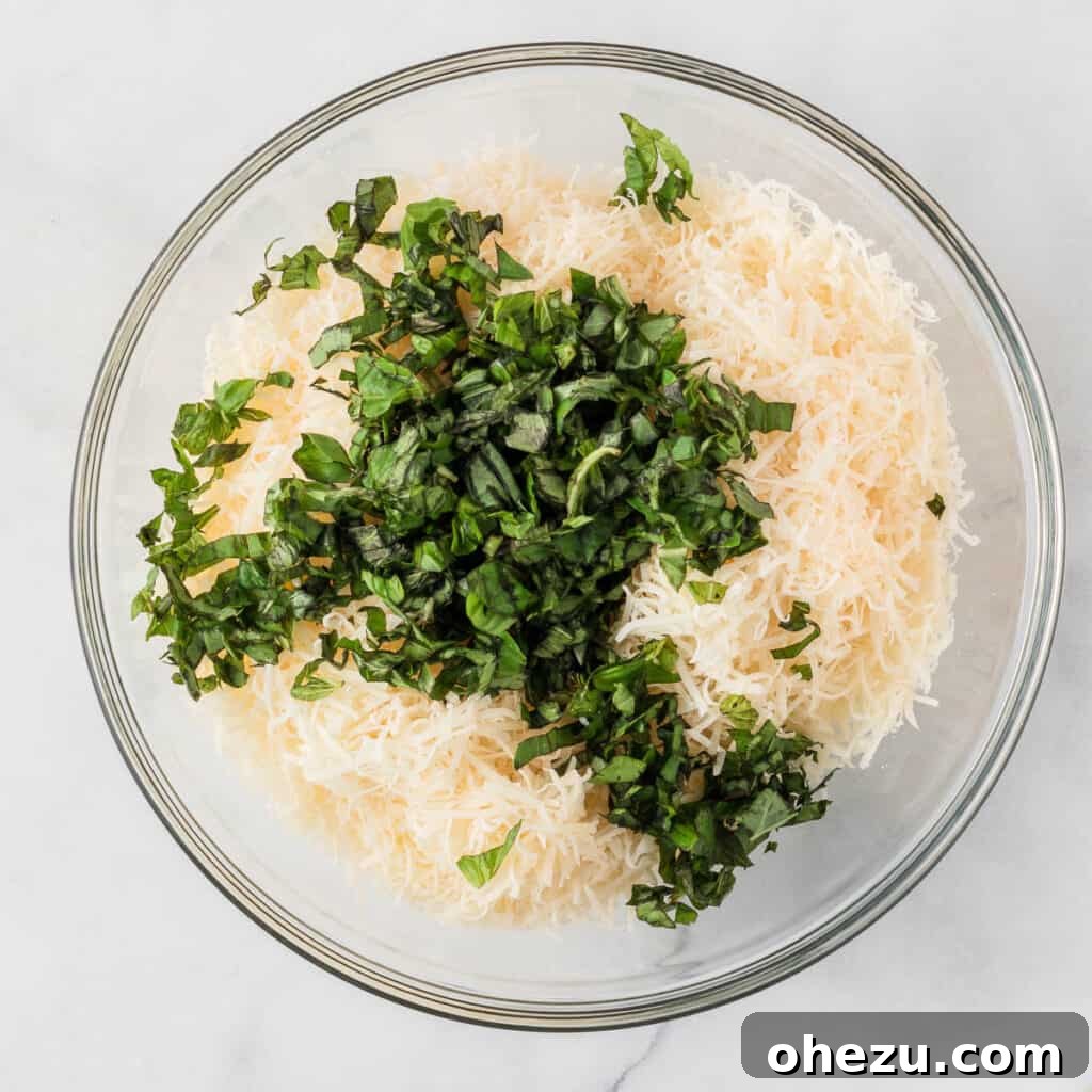 Adding fresh chopped basil and grated parmesan cheese to a bowl of ricotta cheese, preparing the creamy layer for the baked ziti.