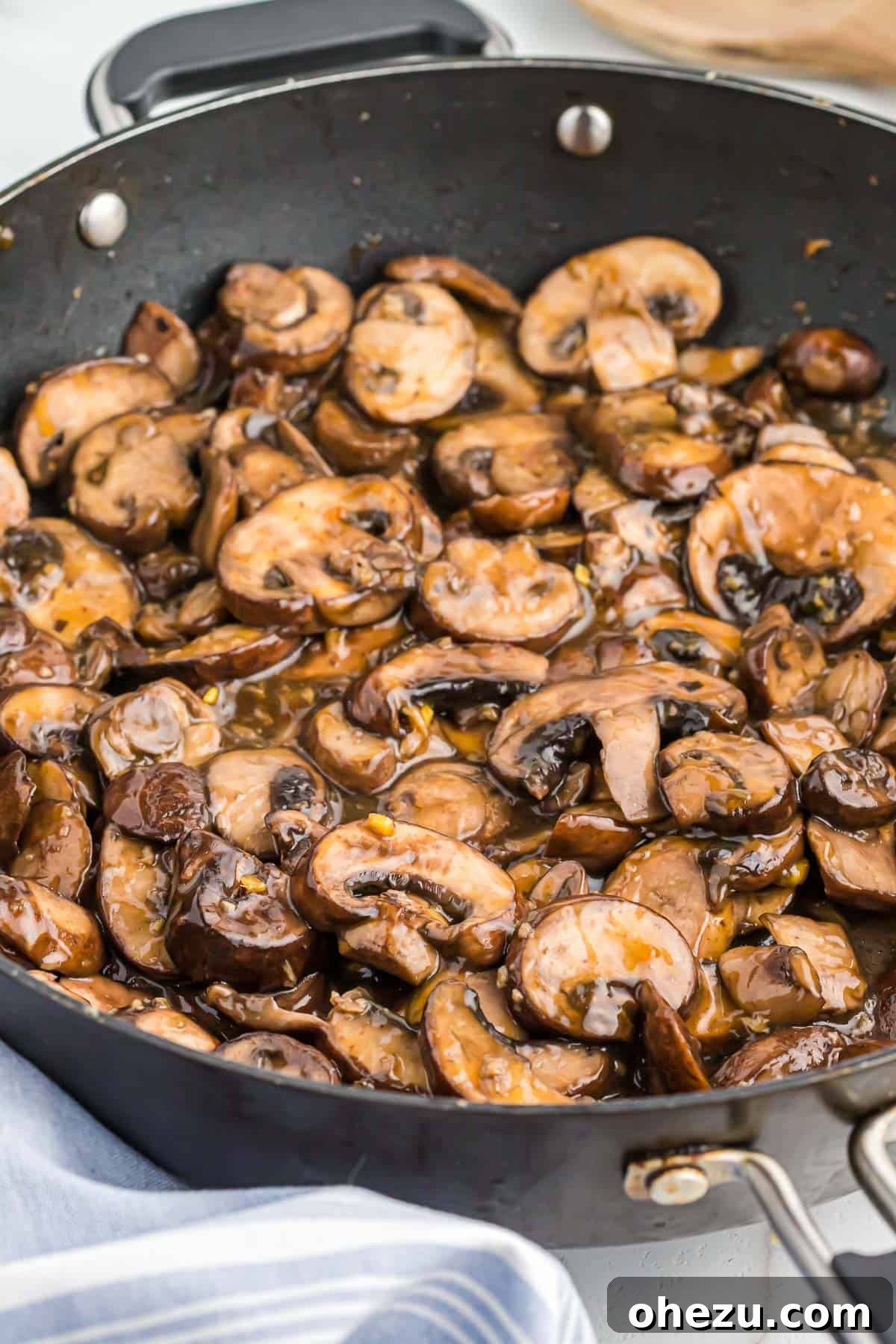 A close-up view of teriyaki fried mushrooms actively cooking and steaming in a skillet, showcasing their glossy coating.